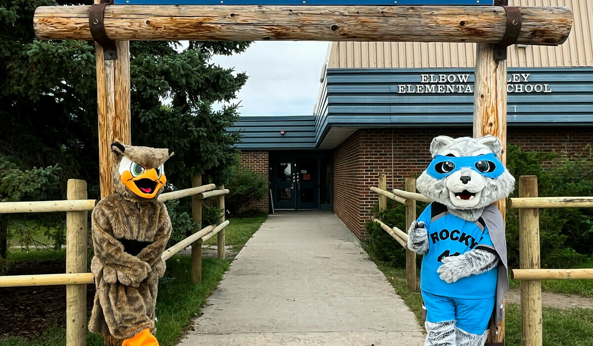 Picture of the entry way to Elbow Valley School. Elbow Valley mascot and RVS mascot lean against the archway.